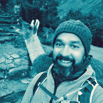 Ferdie Ahmed in a woolly hat on a mountain trail, with a llama right behind him